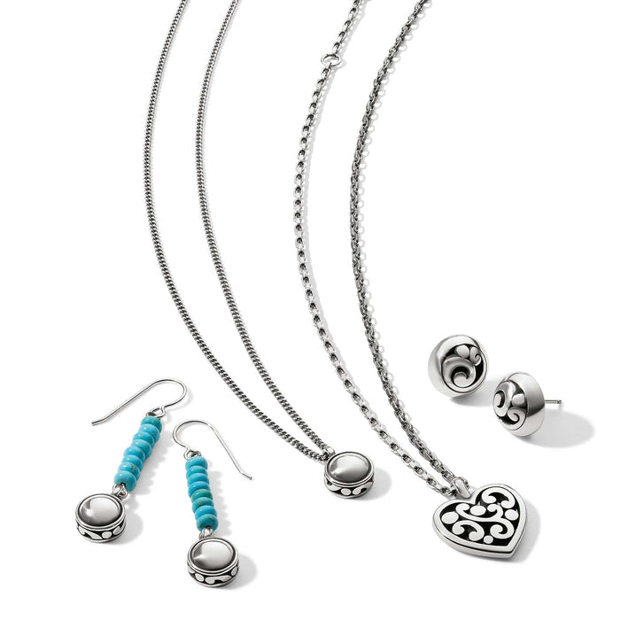 Brighton jewelry set styled with silver-tone necklaces, turquoise drop earrings, and scrollwork heart pendant on white background