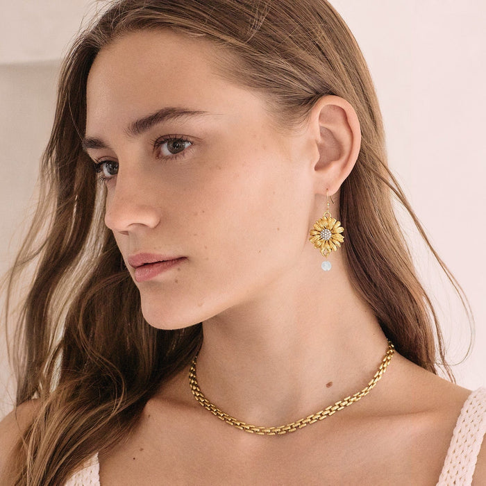 Model wearing Brighton gold-plated sunflower drop earrings with crystal centers and pale blue beads, styled with a Brighton chain necklace
