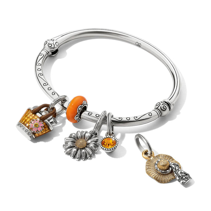 Brighton silver-plated bangle bracelet with floral, daisy, straw hat, and orange enamel crystal charms on a white background