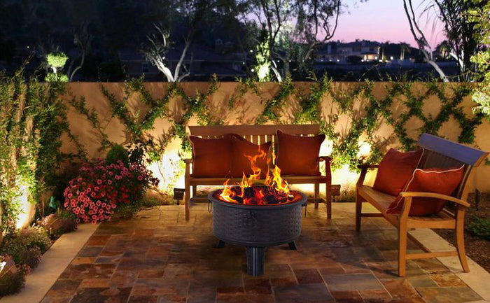 Outdoor patio with fire pit, chairs, and decorative plants at dusk.
