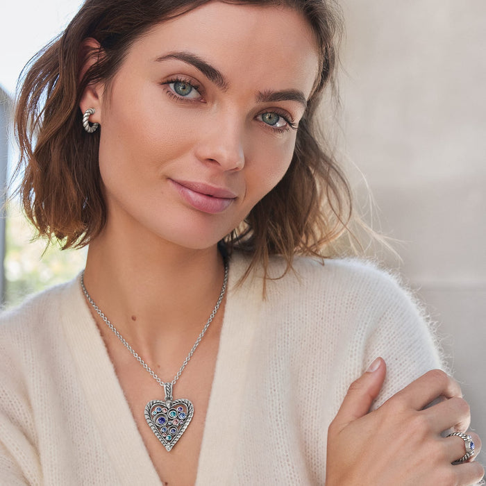 Model wearing a Brighton silver-plated heart pendant necklace with multicolored crystals paired with matching twisted hoop earrings
