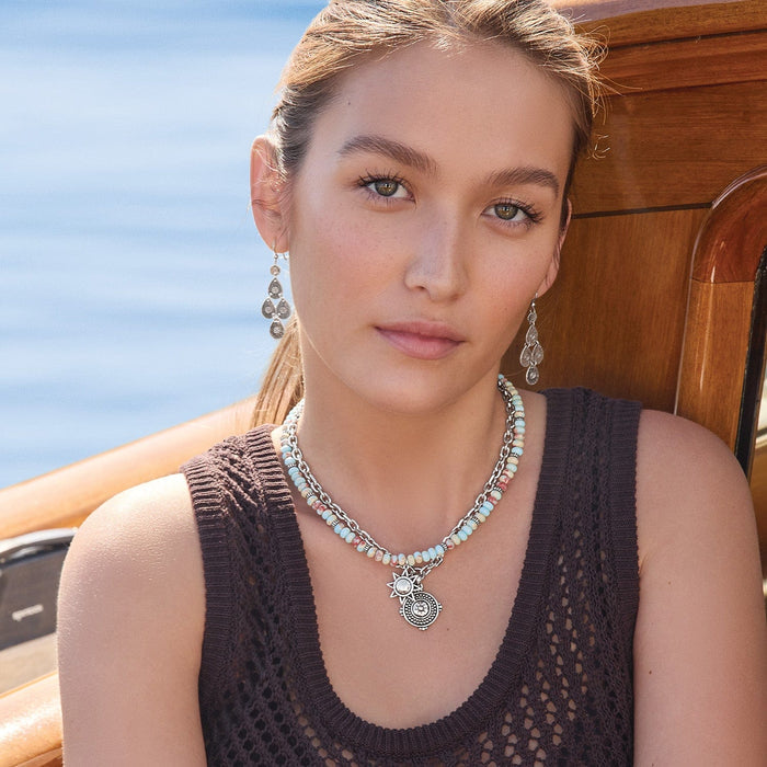 Model wearing a Brighton silver-plated layered necklace with multicolored beads and ornate medallion charms paired with chandelier earrings
