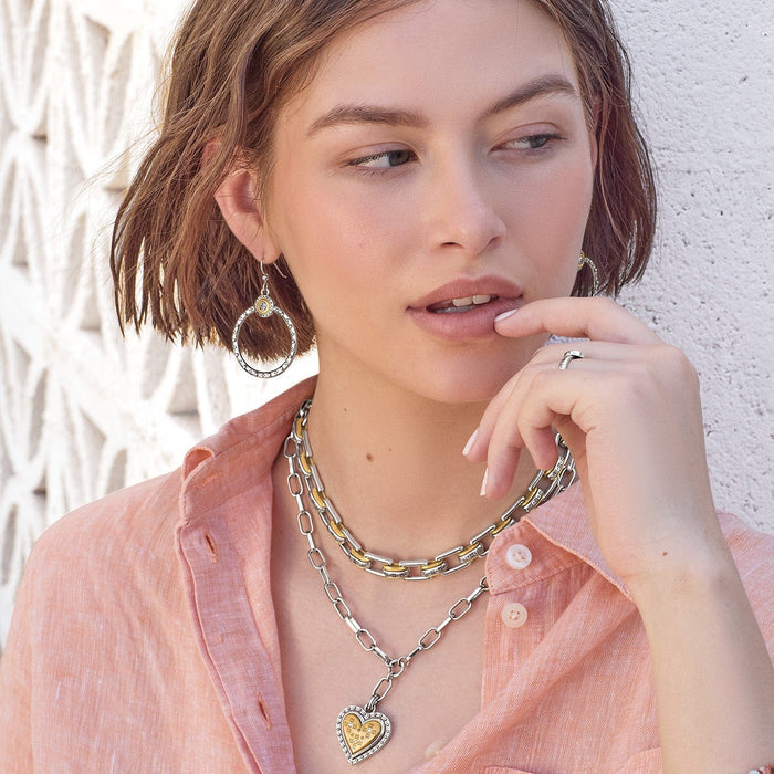 Model wearing a Brighton two-tone heart pendant necklace layered with chain link styles and coordinating Brighton accessories