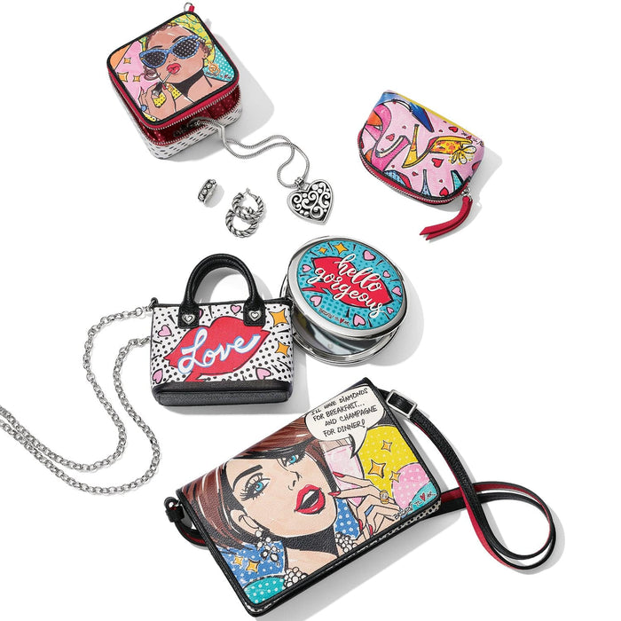Brighton handbag collection styled with pop-art illustrated prints, silver heart pendant necklace, and other accessories on white background