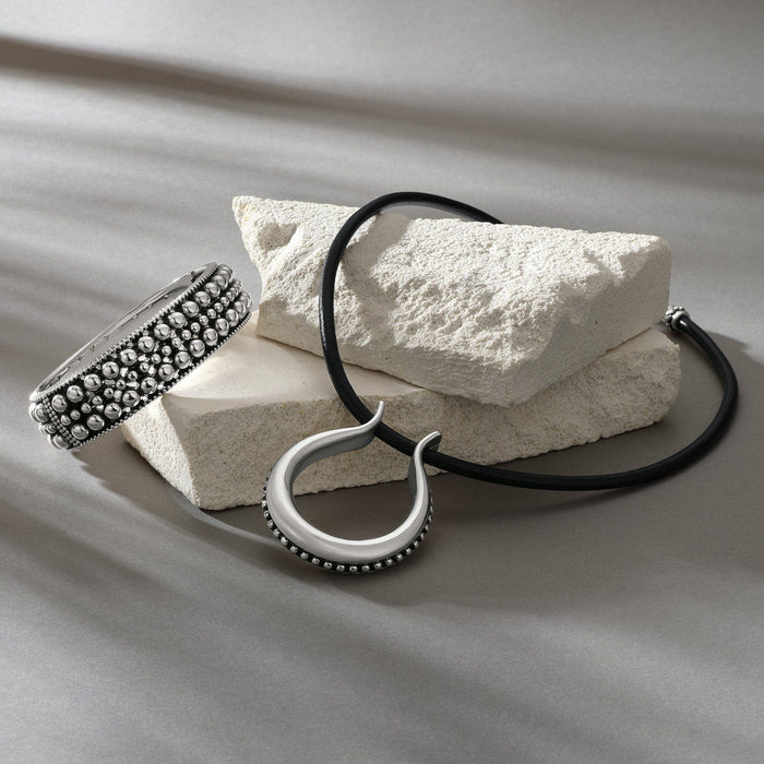 Brighton silver-plated beaded cuff bracelet styled with a leather pendant necklace on white stones and neutral fabric