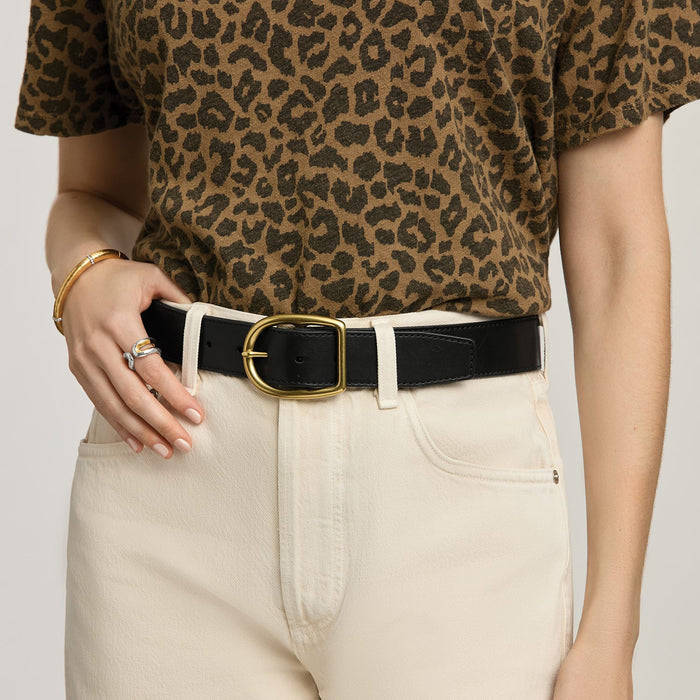 Model wearing a Brighton black leather belt with oval gold-tone buckle, paired with cream jeans