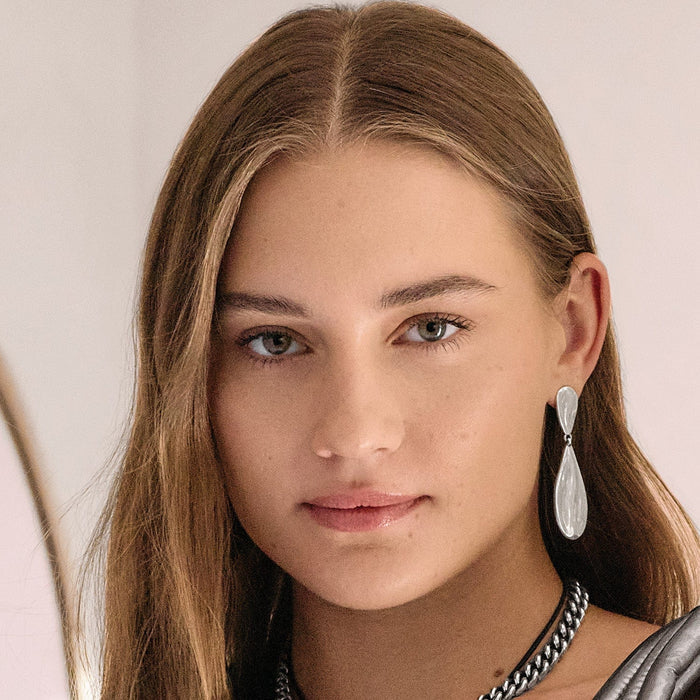 Model wearing Brighton silver-plated drop earrings with elongated hourglass shape, paired with a Brighton silver chain necklace