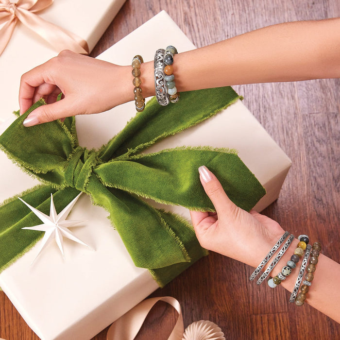 Model wearing Brighton silver-plated bracelets with multicolor beaded strands and scrollwork bangles, holding a green ribbon gift