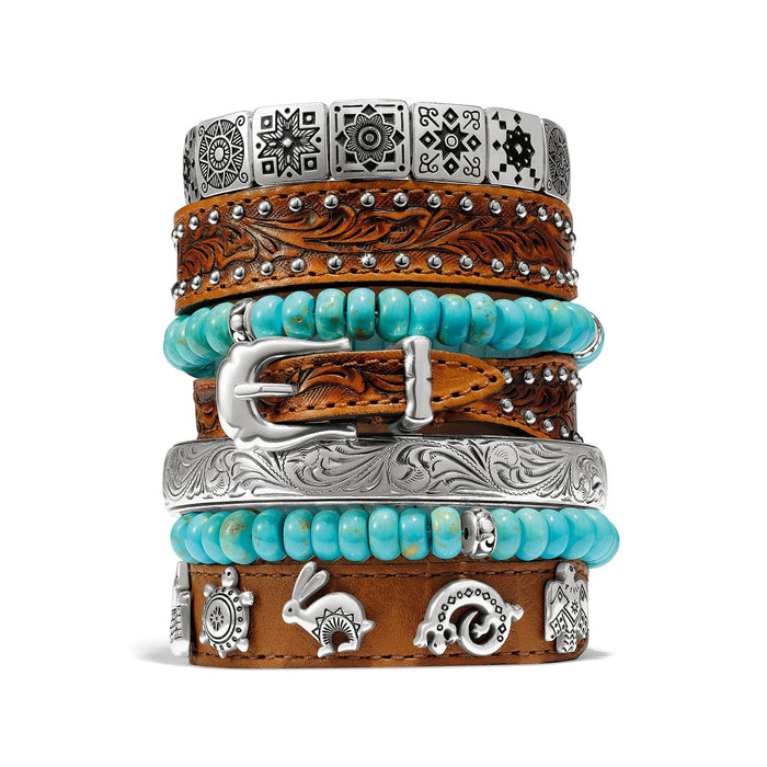 Brighton stacked bracelets with tooled leather, turquoise beads, silver-plated engraved bangle, and southwestern charms on a white background
