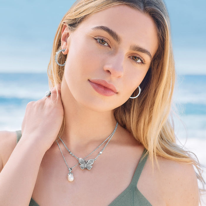Model wearing a Brighton silver-plated butterfly necklace with rice pearl pendant and coordinating Brighton accessories