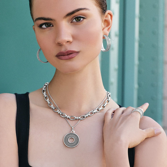 Model wearing Brighton silver-plated hoop earrings with layered chain necklace, circular medallion pendant, and coordinating ring