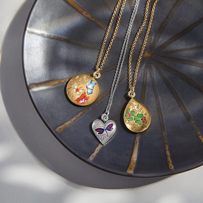 Brighton lockets styled with enamel butterfly, ladybug, and floral designs in gold and silver finishes on a metal tray