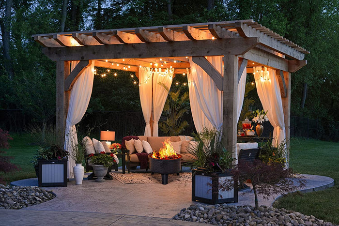 Outdoor gazebo with curtains, fire pit, and decorative elements in a garden setting.