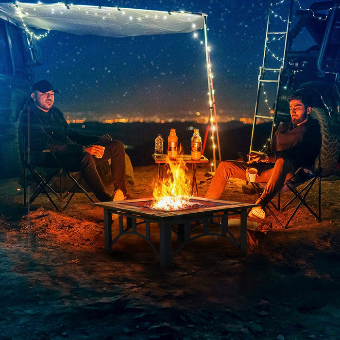 Two people sitting around a campfire at night with string lights and a ladder in the background.