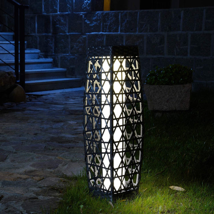 Decorative outdoor lamp with geometric pattern on a grassy area at night.