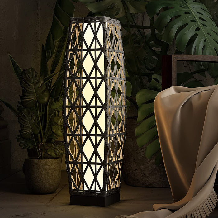 Decorative floor lamp with geometric pattern in a dimly lit room with plants and a blanket.