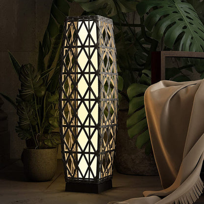 Decorative floor lamp with geometric pattern in a dimly lit room with plants and a blanket.