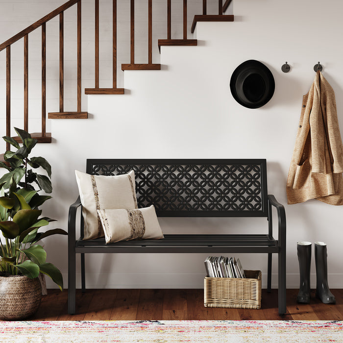 Durable garden bench with a black steel frame and floral lattice design, placed near a staircase and potted plant.