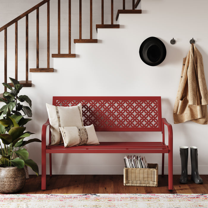 Red garden bench with floral lattice design, placed near a staircase, accompanied by pillows and a plant.