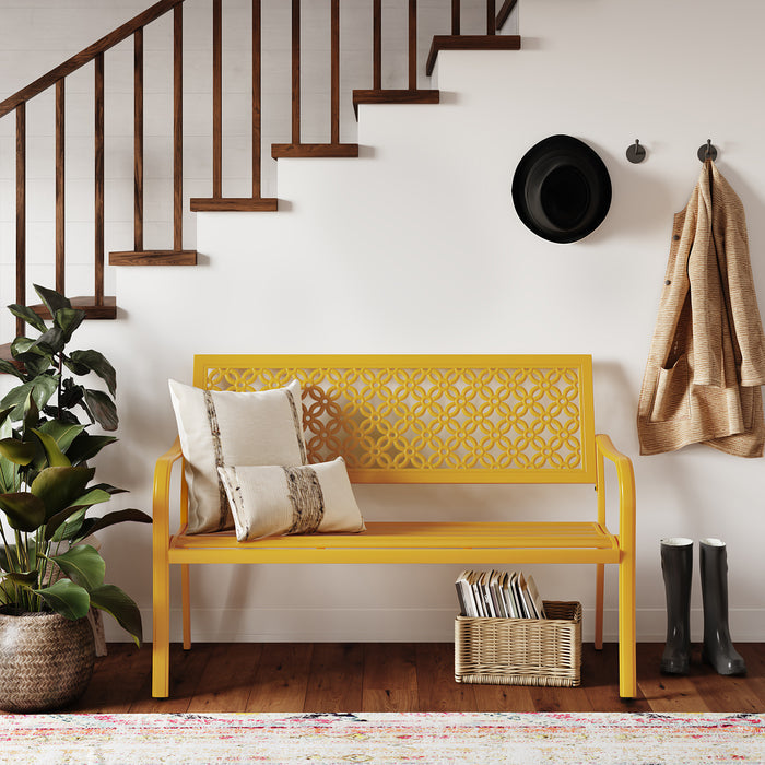 Yellow garden bench with floral lattice design, two pillows, and a plant beside a staircase and wall hooks.