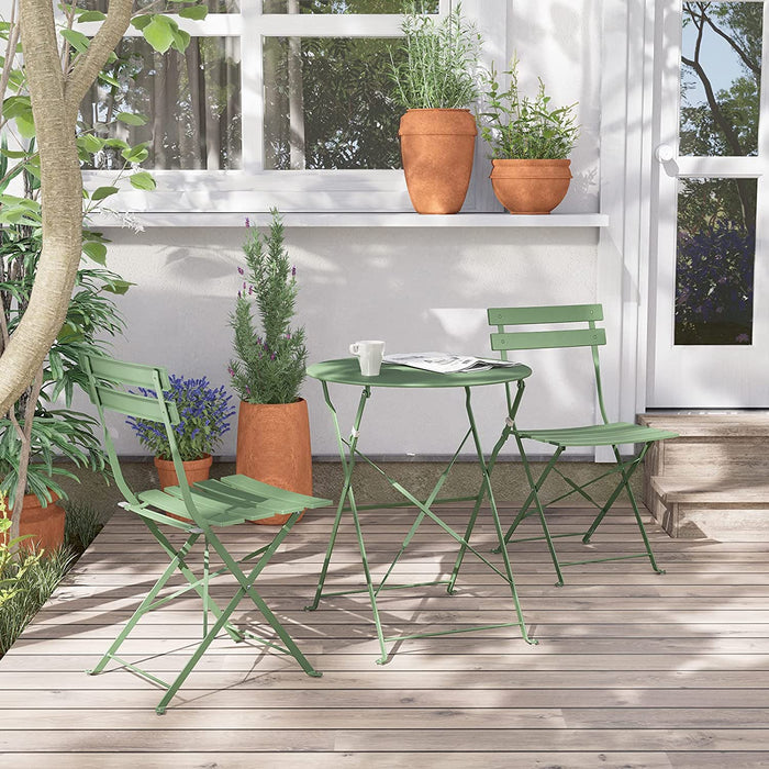 Green outdoor table and chairs on a wooden deck with plants and a white wall in the background.