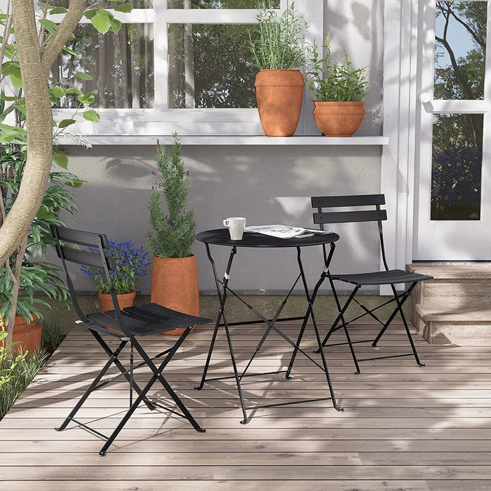 Black metal outdoor table and chairs on a wooden deck with plants and a window in the background.