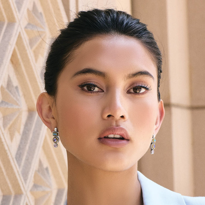 Model wearing Brighton two-tone drop earrings with stacked geometric crystals in blue, purple, and pink hues