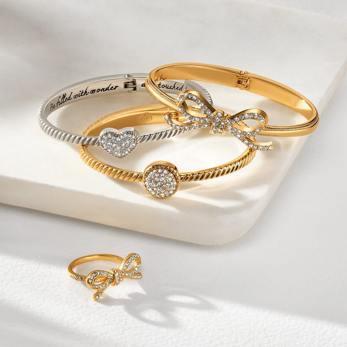 Brighton bangle bracelets styled with a coordinating crystal bow ring in silver-plated and gold-plated finishes on cream surface