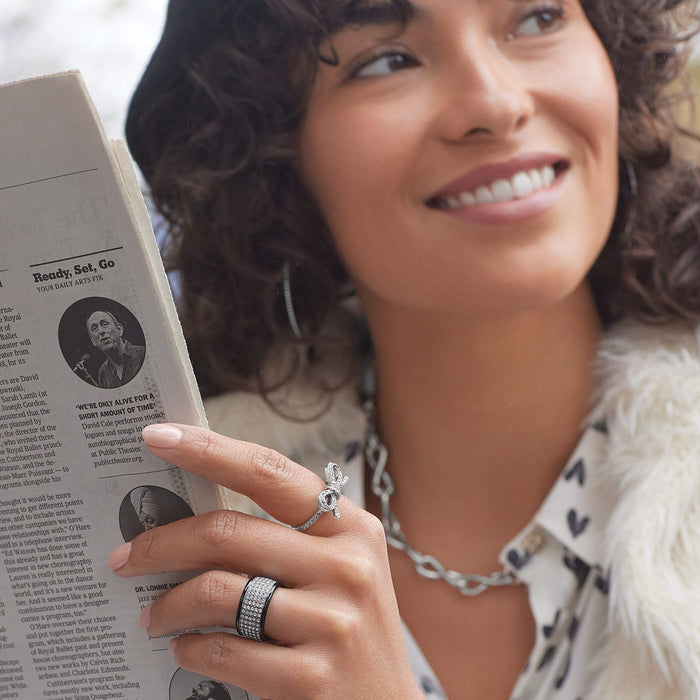 Model wearing a Brighton silver-plated bow ring with crystals and coordinating Brighton accessories while holding a newspaper