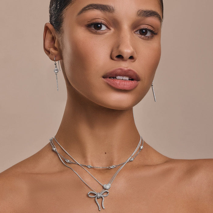 Model wearing Brighton silver-plated drop earrings with crystals and coordinating Brighton accessories including layered necklaces with bow pendant