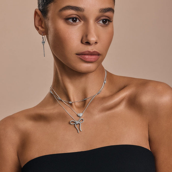 Model wearing Brighton silver-plated layered necklaces with crystal bow and heart pendants paired with crystal drop earrings