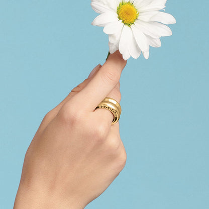 Model wearing a Brighton gold-tone ring with scroll cutout detail, holding a white daisy flower