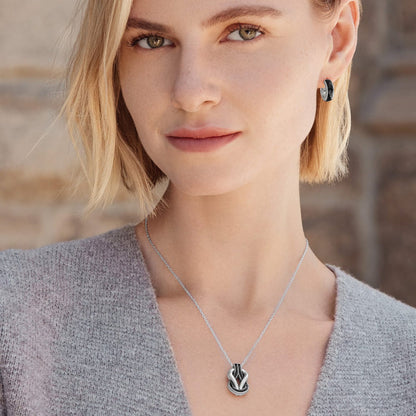 Model wearing a Brighton silver-plated pendant necklace with black enamel knot design paired with matching hoop earrings