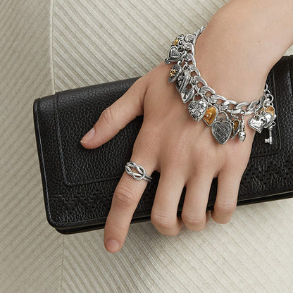 Model wearing a Brighton silver-plated heart charm bracelet paired with a silver-plated knot ring, holding a black handbag