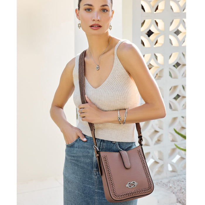 Model with a Brighton mauve leather crossbody handbag featuring whipstitch trim and braided strap, styled with coordinating Brighton accessories