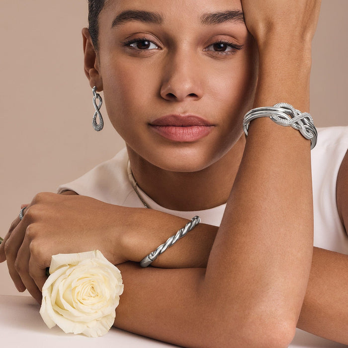 Model wearing Brighton silver-plated infinity drop earrings with crystals and coordinating Brighton bracelets on both wrists