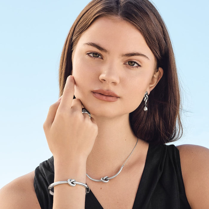 Model wearing a Brighton silver knot necklace paired with matching knot bangle bracelet, drop earrings, and ring