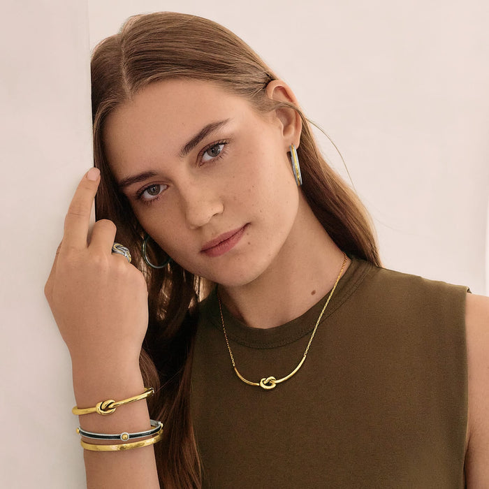 Model wearing a Brighton gold-tone knot necklace with coordinating Brighton accessories including hoop earrings and stacked bangles