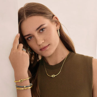 Model wearing a Brighton gold-tone knot necklace with coordinating Brighton accessories including hoop earrings and stacked bangles