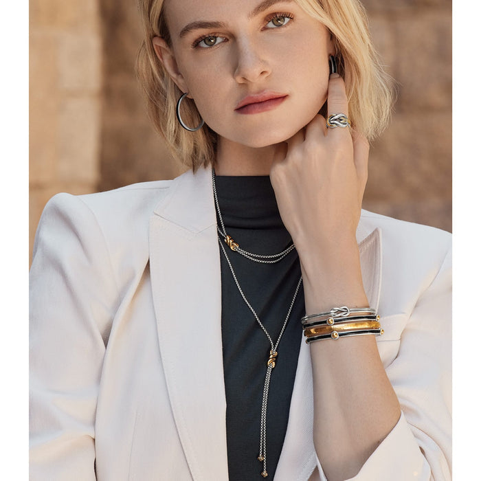 Model wearing Brighton two-tone hoop earrings with matching knot ring, layered necklaces, and stacked bangle bracelets