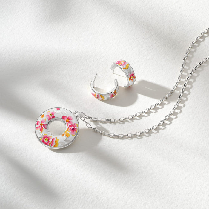 Brighton silver-plated pendant necklace and hoop earrings with pink floral enamel design styled together on white fabric