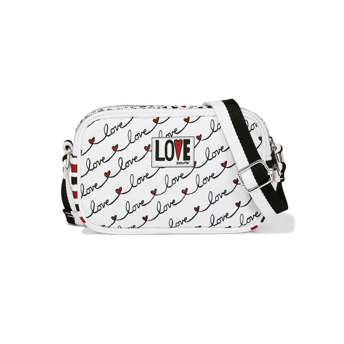 Brighton crossbody handbag with white love script print, red hearts, striped adjustable strap, and logo patch on a white background