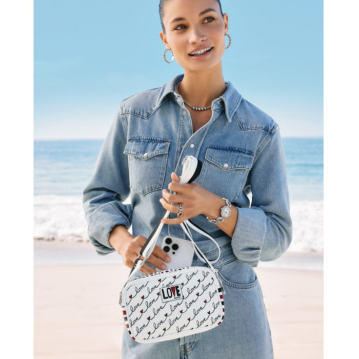 Model with a Brighton white crossbody handbag featuring black love script print and red heart accents