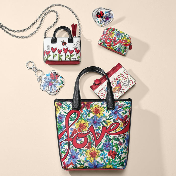 Brighton floral love-print tote styled with coordinating mini handbag, wallets, and other accessories on a neutral background