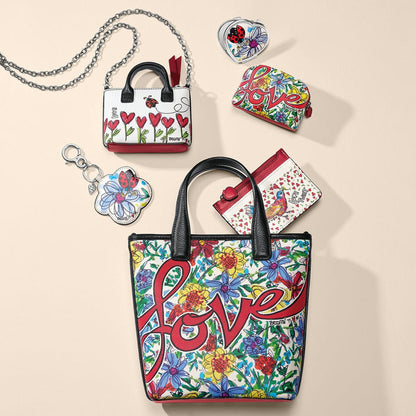 Brighton floral love-print tote styled with coordinating mini handbag, wallets, and other accessories on a neutral background