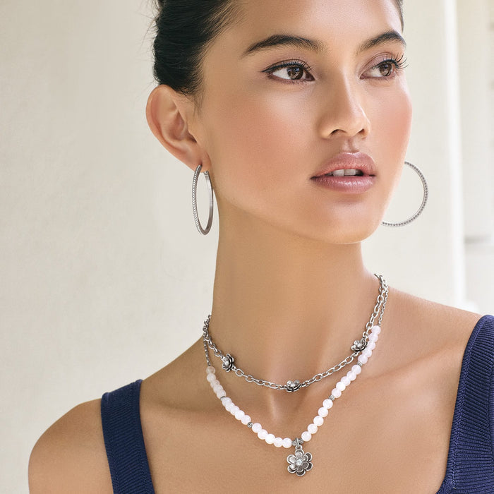 Model wearing Brighton layered silver-plated necklaces with white dyed jade beads, flower accents, and coordinating Brighton hoop earrings