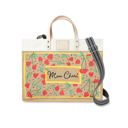 Brighton tote handbag with cherry and heart print, Mon Cheri label, and striped crossbody strap on a white background