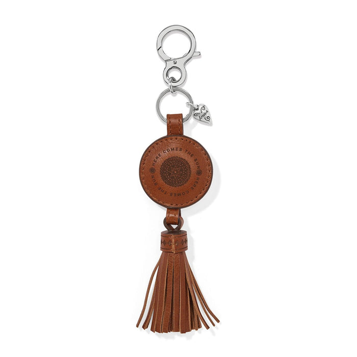 Brighton brown leather bag charm with engraved sun medallion, tassel, and silver-tone heart charm on a white background