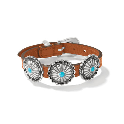 Brighton bracelet with brown leather strap, three silver-plated concho medallions, turquoise stones, and buckle closure on a white background