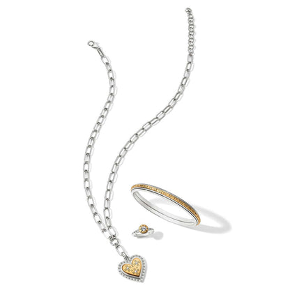 Brighton jewelry set styled with silver chain necklace, heart pendant, two-tone bangle, and crystal ring on white